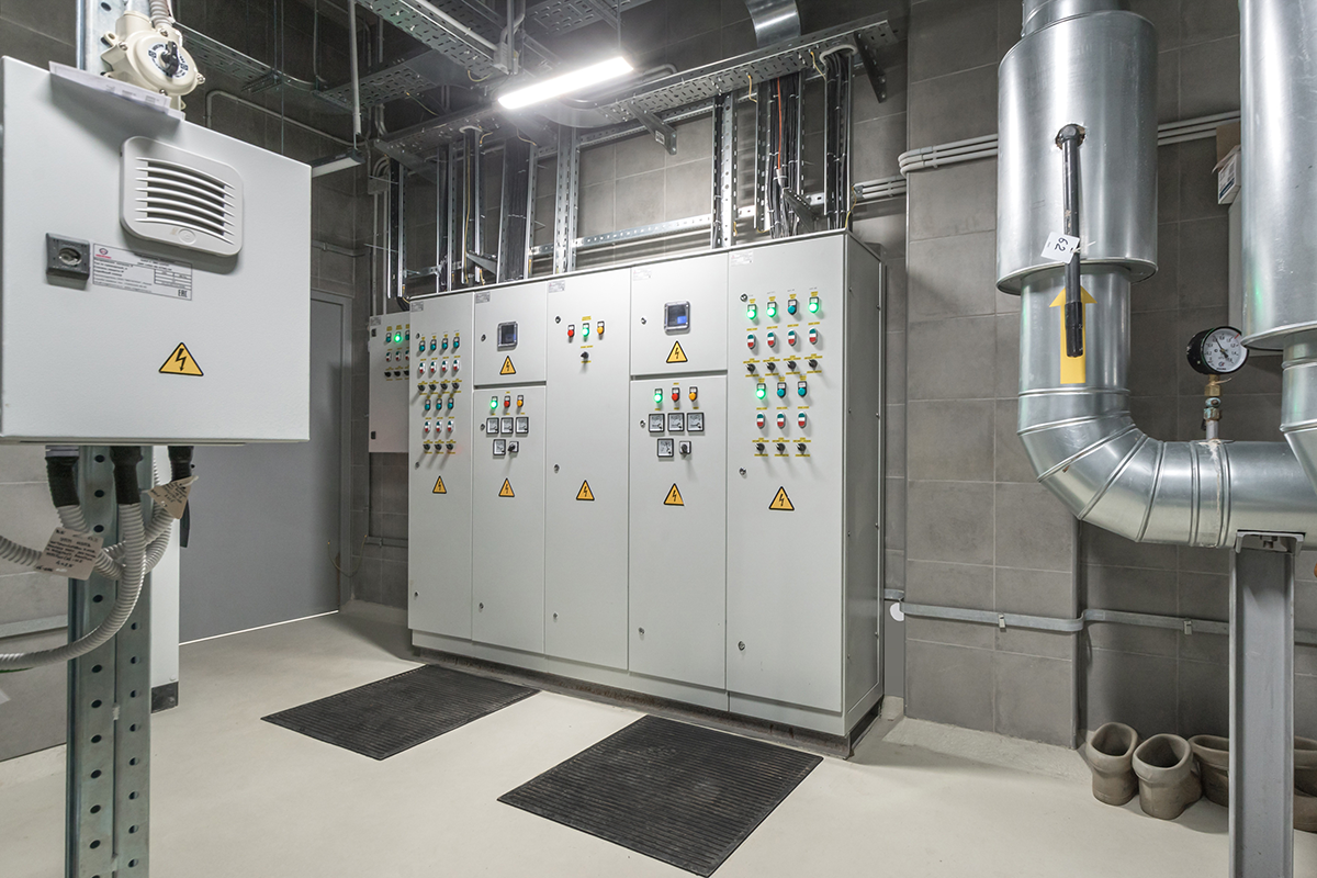 Electrical control room with industrial switchgear cabinets, warning labels, and conduit piping.