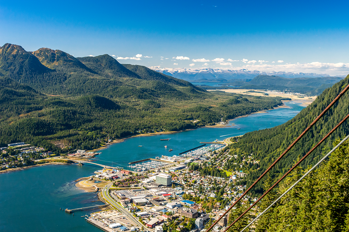 Aerial view of downtown Juneau, Alaska with waterways, forested mountains, and harbor below.