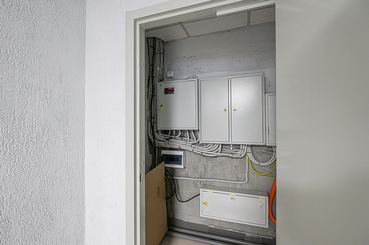 Multiple residential electrical breaker panels mounted in a utility room with exposed conduit and wiring